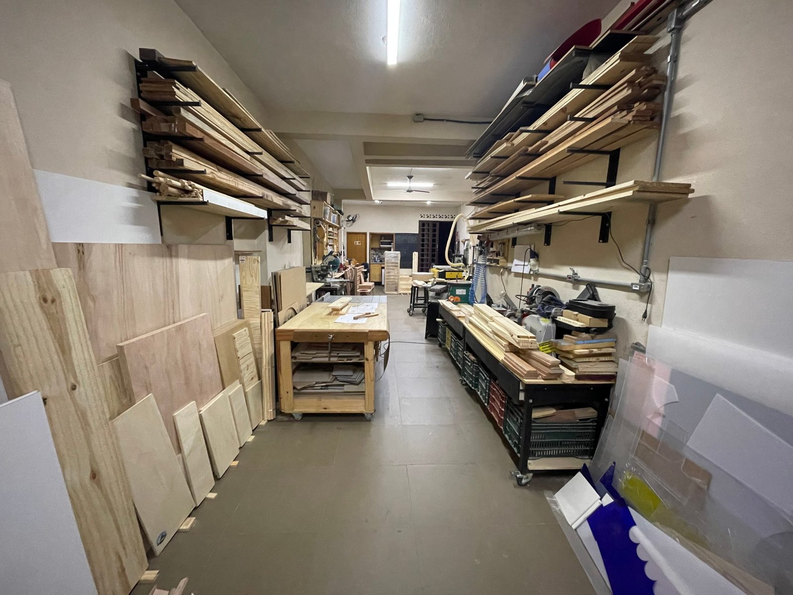 Interior do ateliê da Omni Fabricações, com estoque de madeira e bancadas de trabalho