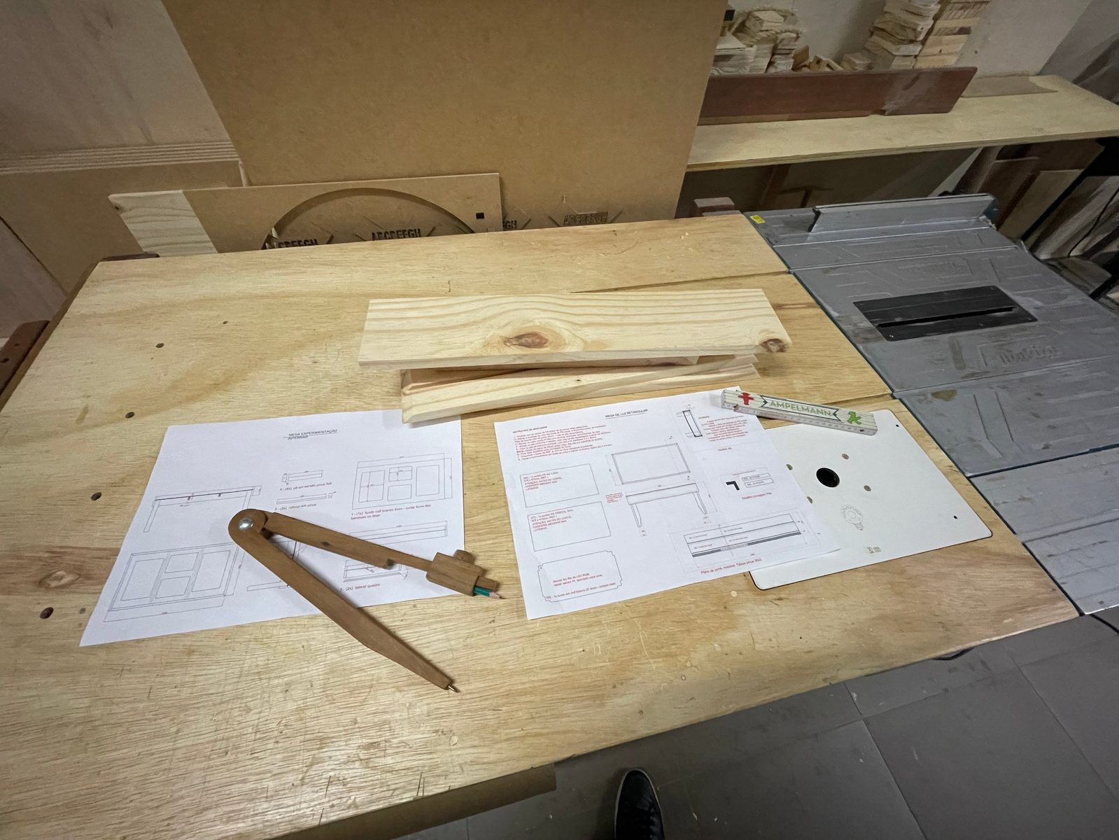 Projeto técnico desenhado à mão, com peças de madeira e instrumentos de precisão sobre a bancada